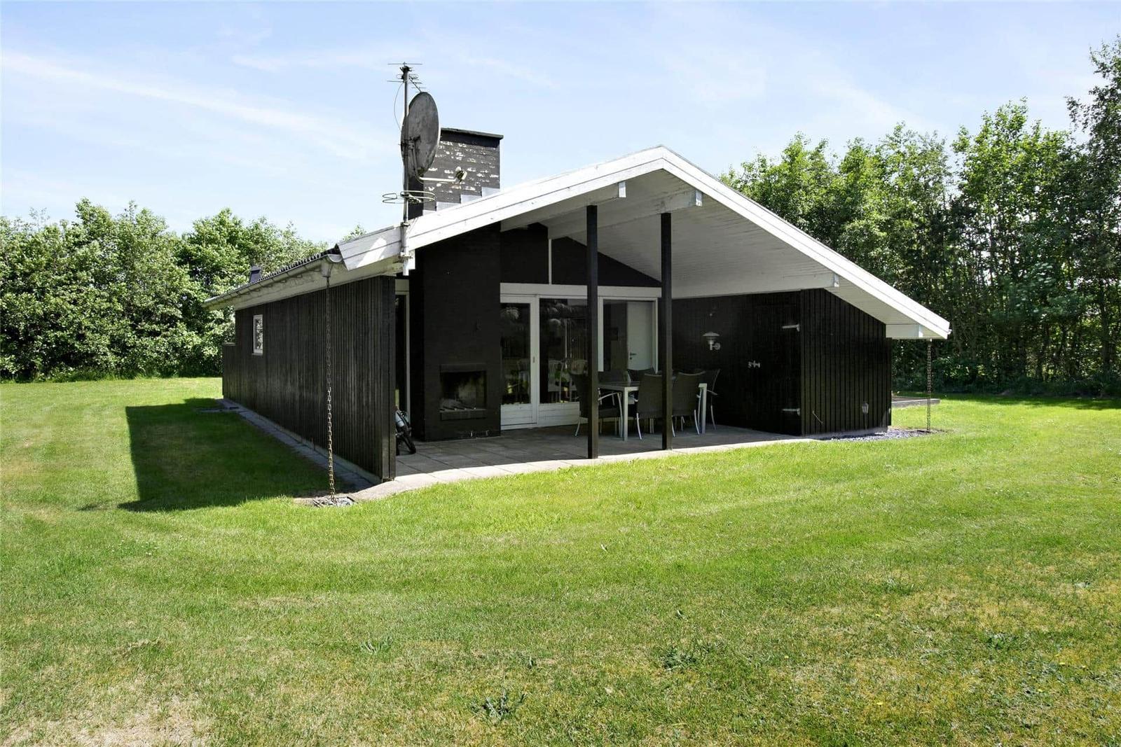 Moderne Holzhütte mit Terrasse, Grill und Satellitenanlage. Umgeben von Gras und Bäumen.