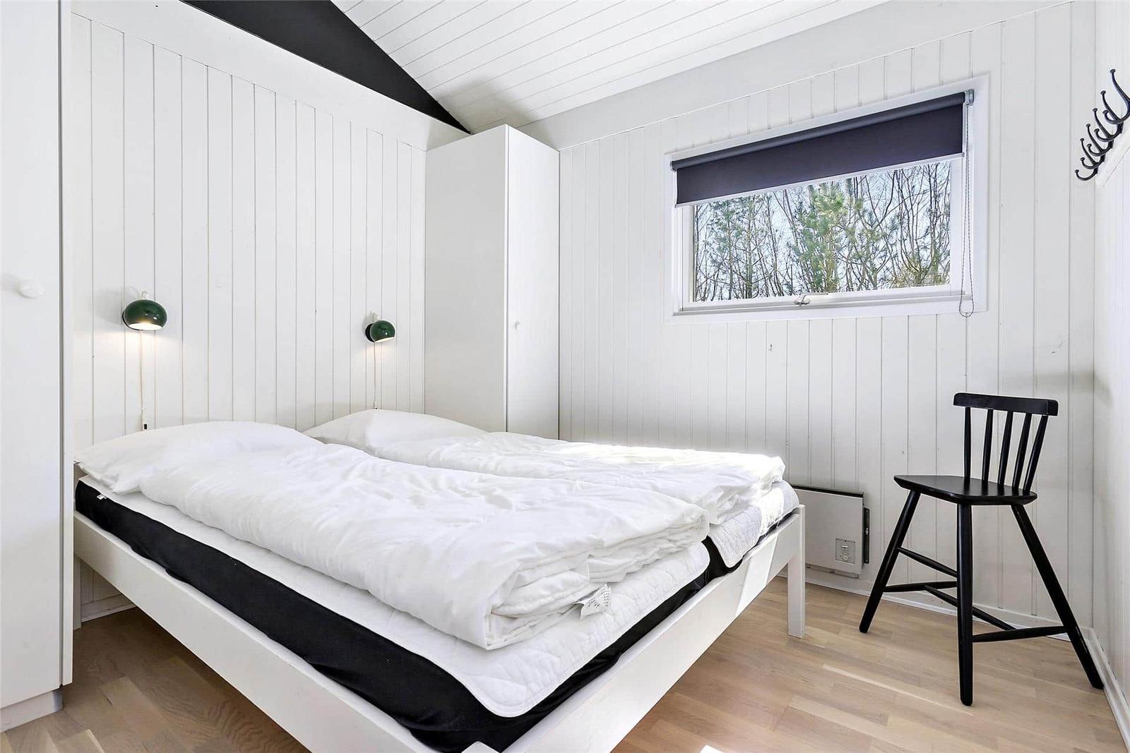 Schlafzimmer mit weißem Bett, Holzboden und Fenster mit Blick auf Bäume.