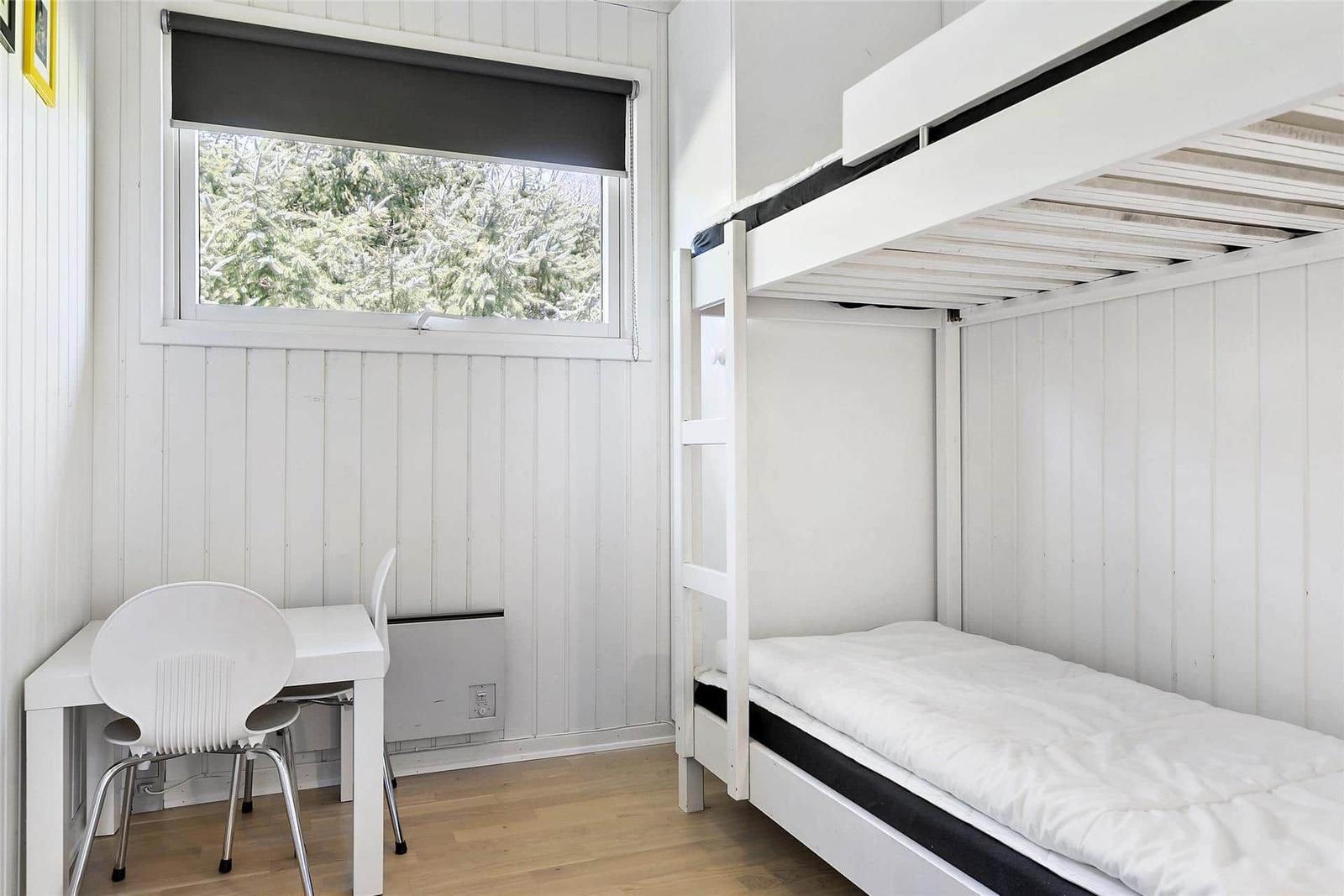 Zimmer mit Doppelbett, Schreibtisch und Fenster mit Blick auf Bäume.