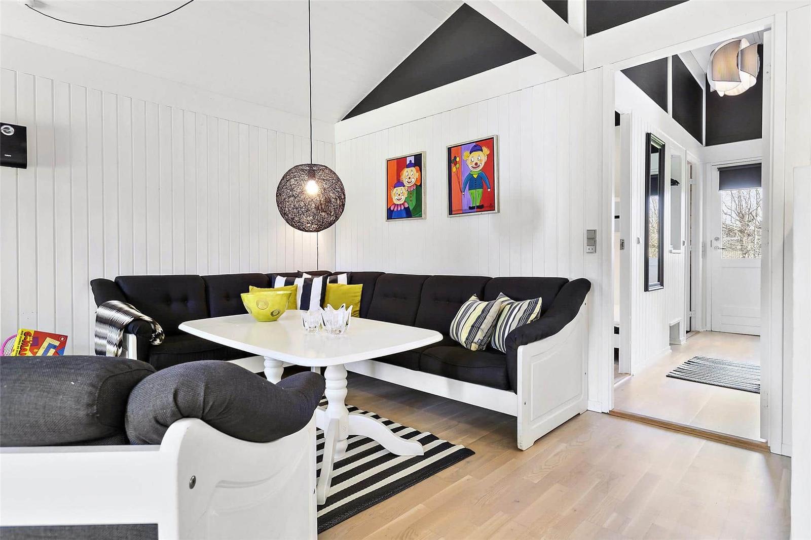 Wohnzimmer mit schwarzer Sofa, weißem Tisch und Wandbildern.