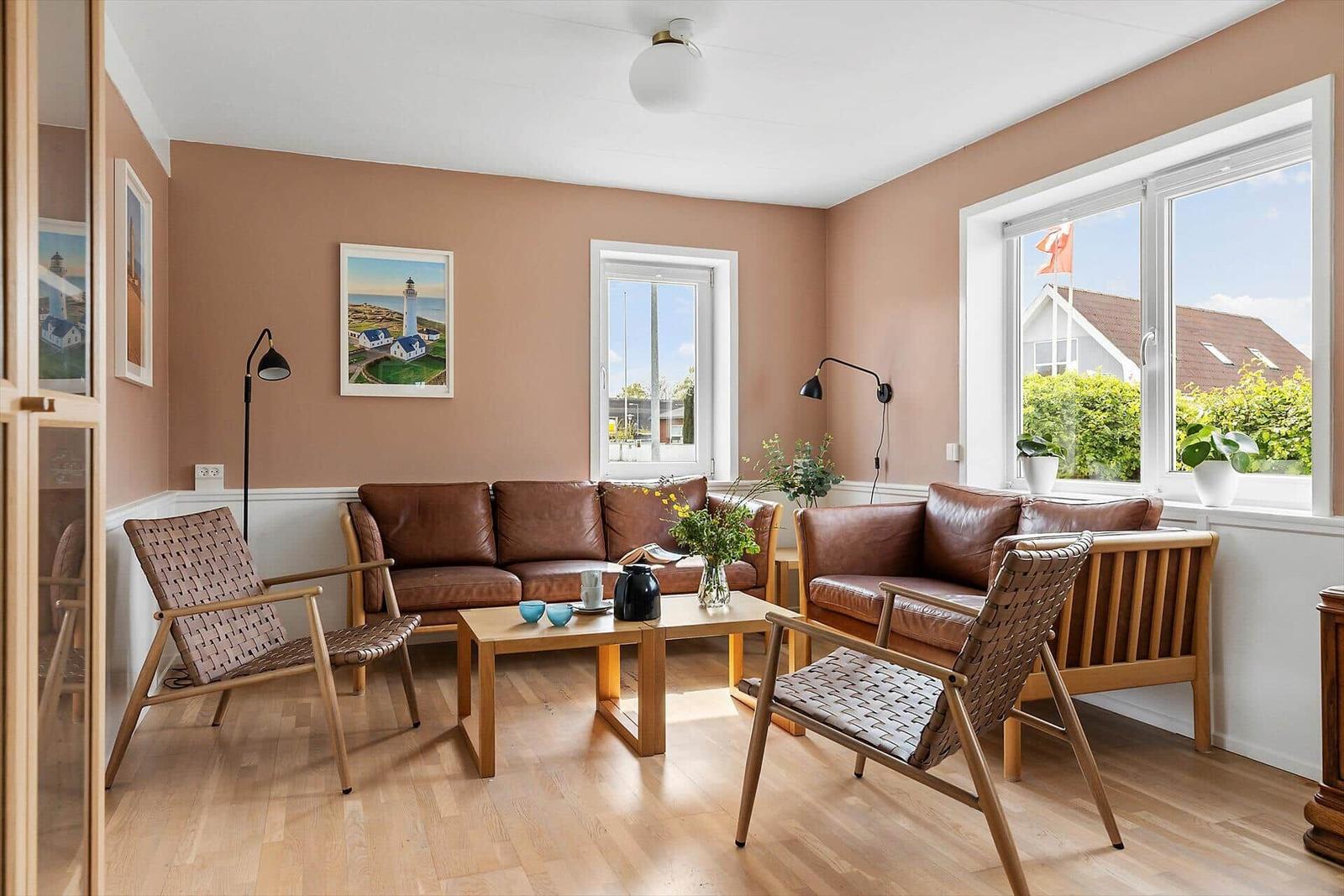Wohnzimmer mit braunen Ledersofas, Holzmöbeln und großen Fenstern.