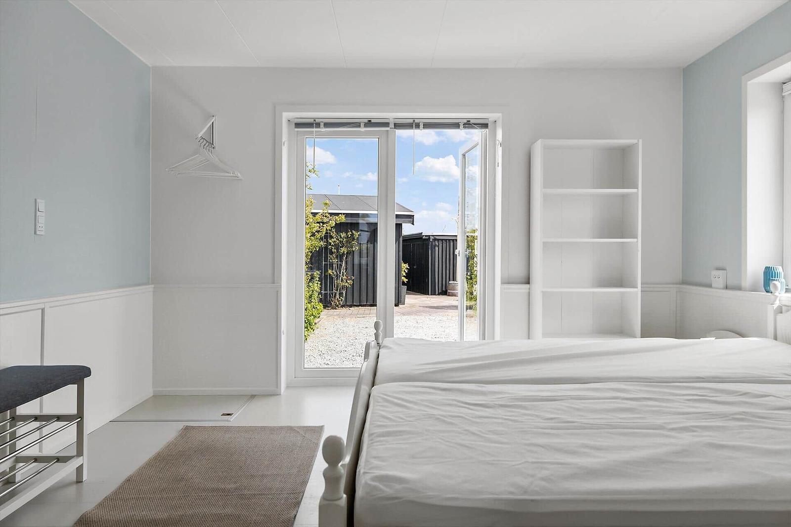Schlafzimmer mit Doppelschlafcouch, Fenster zum Garten und weißen Möbeln.