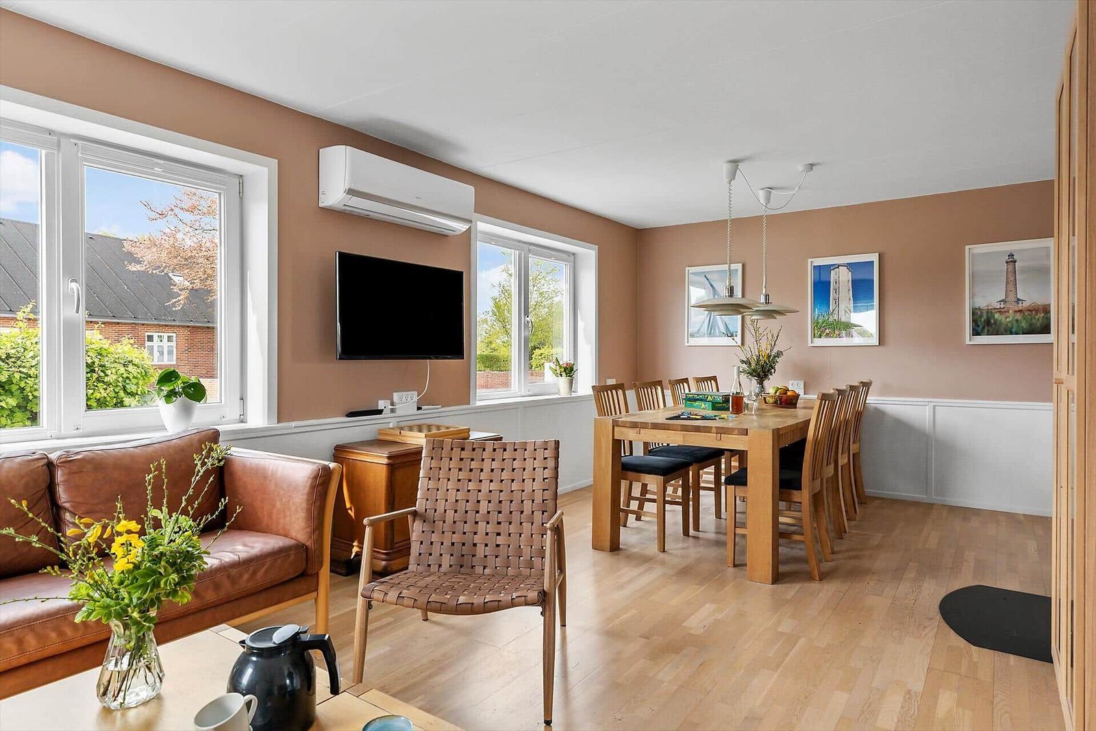 Wohn- und Essbereich mit Holzboden, Sofa, Esstisch und Fenstern.