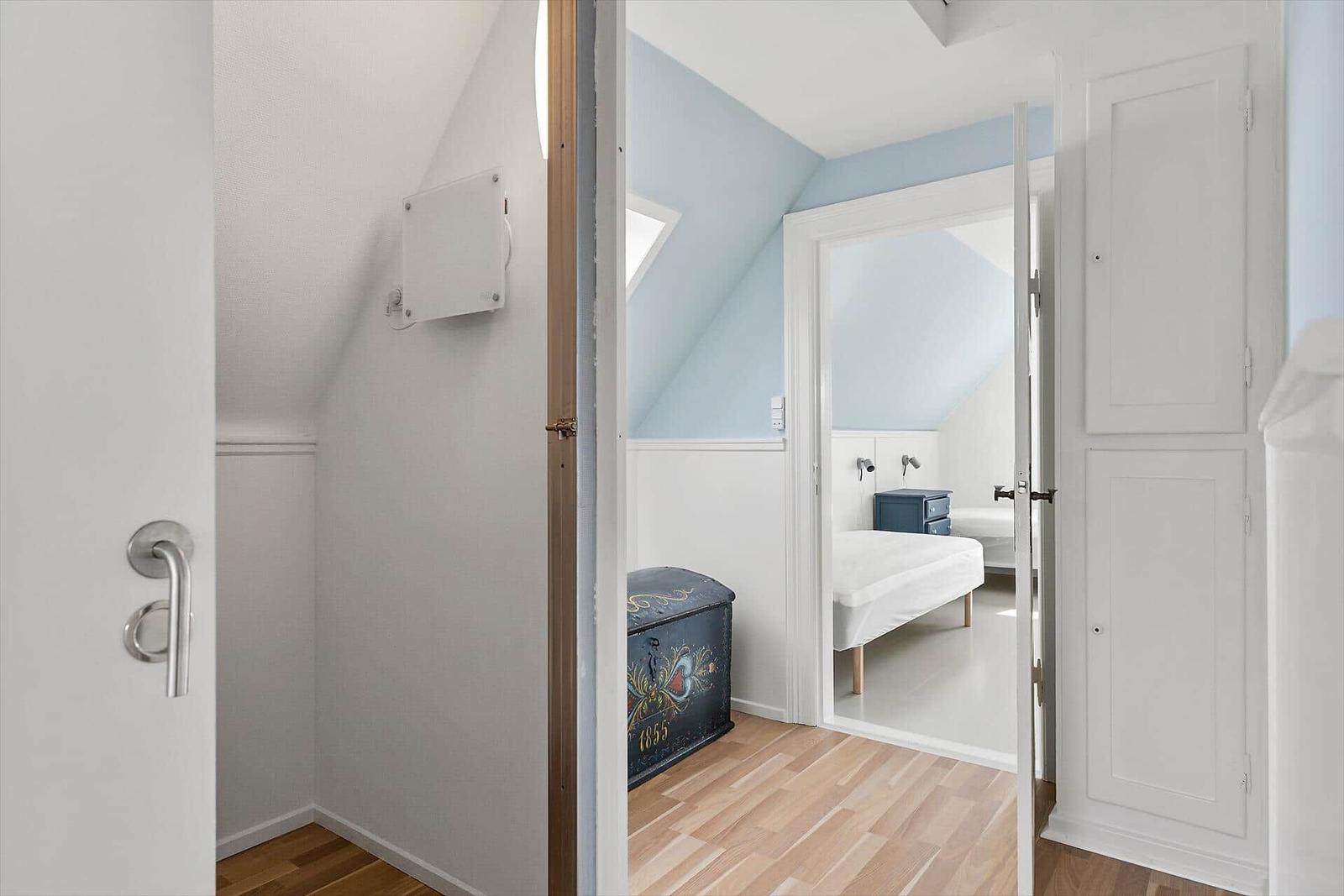 Schlafzimmer mit blauen Wänden und Holzboden. Antiker Koffer und Bett sichtbar.