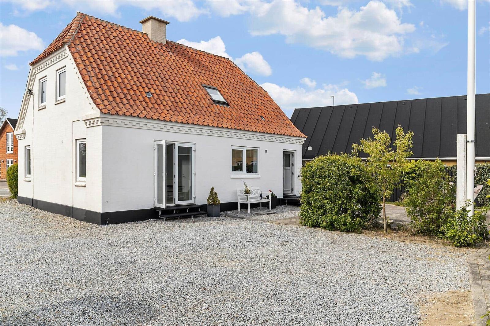 Weiße Ferienhaus mit rotem Ziegeldach und Terrasse im Vorgarten.