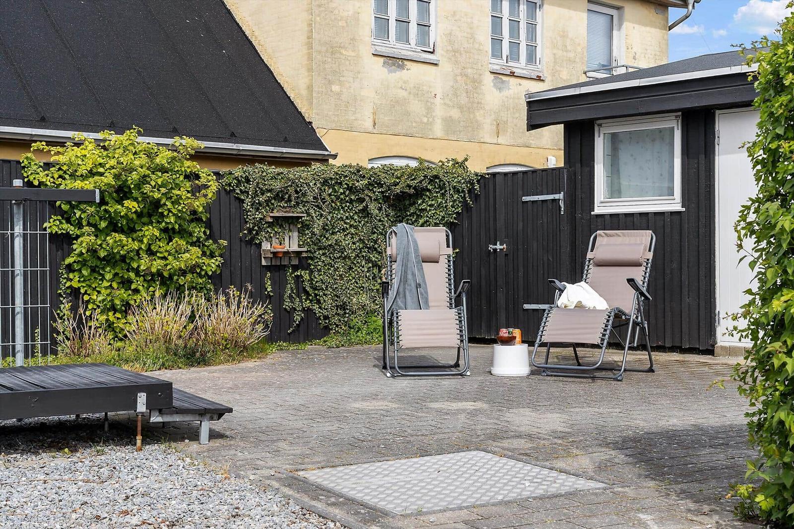 Hinterhof mit zwei Liegestühlen, Pflanzen und Steinplatten.