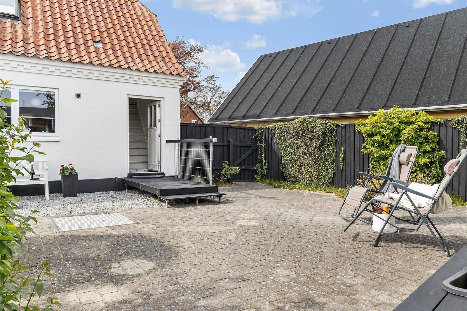 Hinterhof mit Terrasse, Sitzgelegenheiten und Gartenzaun.