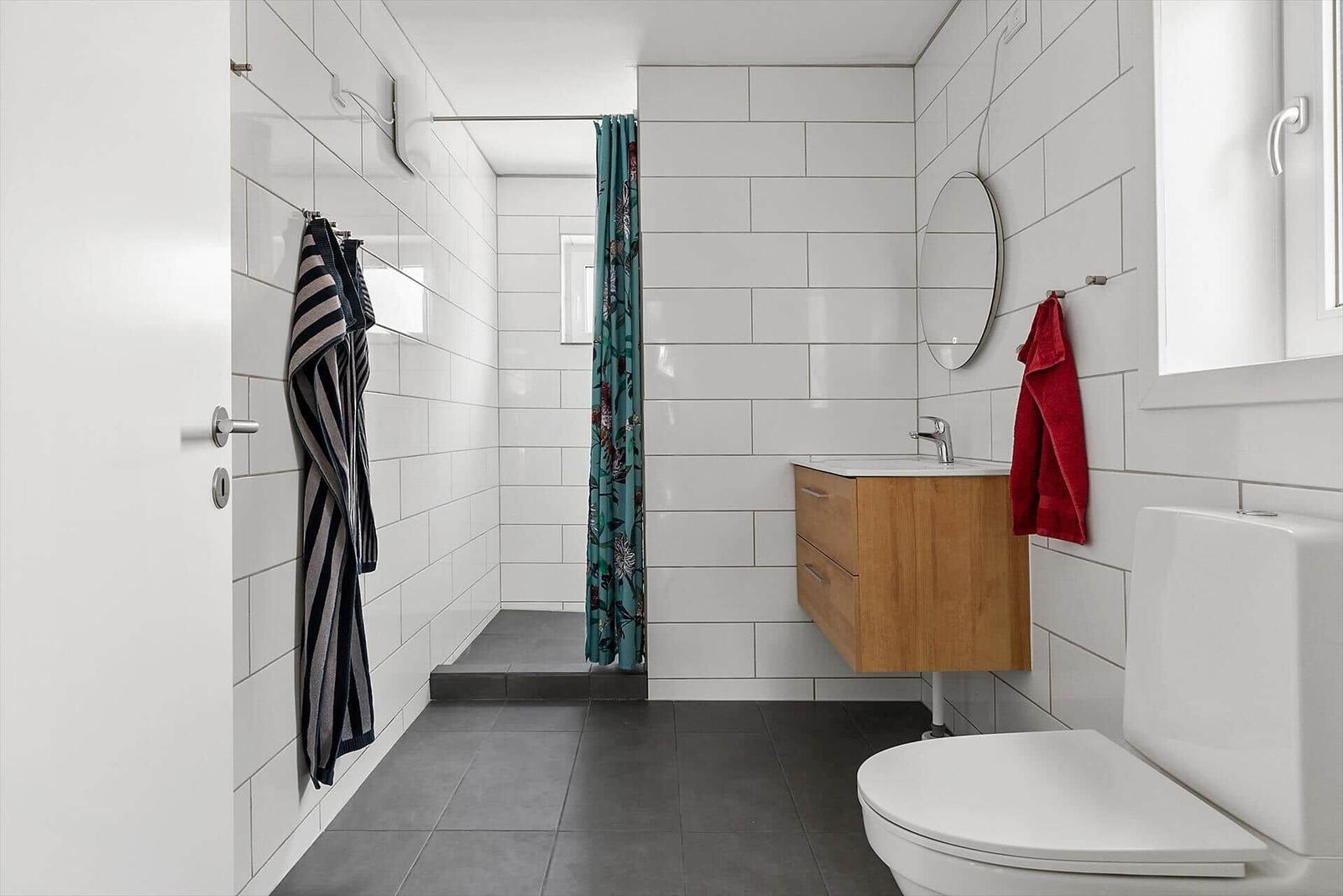 Badezimmer mit Dusche, Waschbecken und Toilette. Weiße Fliesen und Holzschrank.