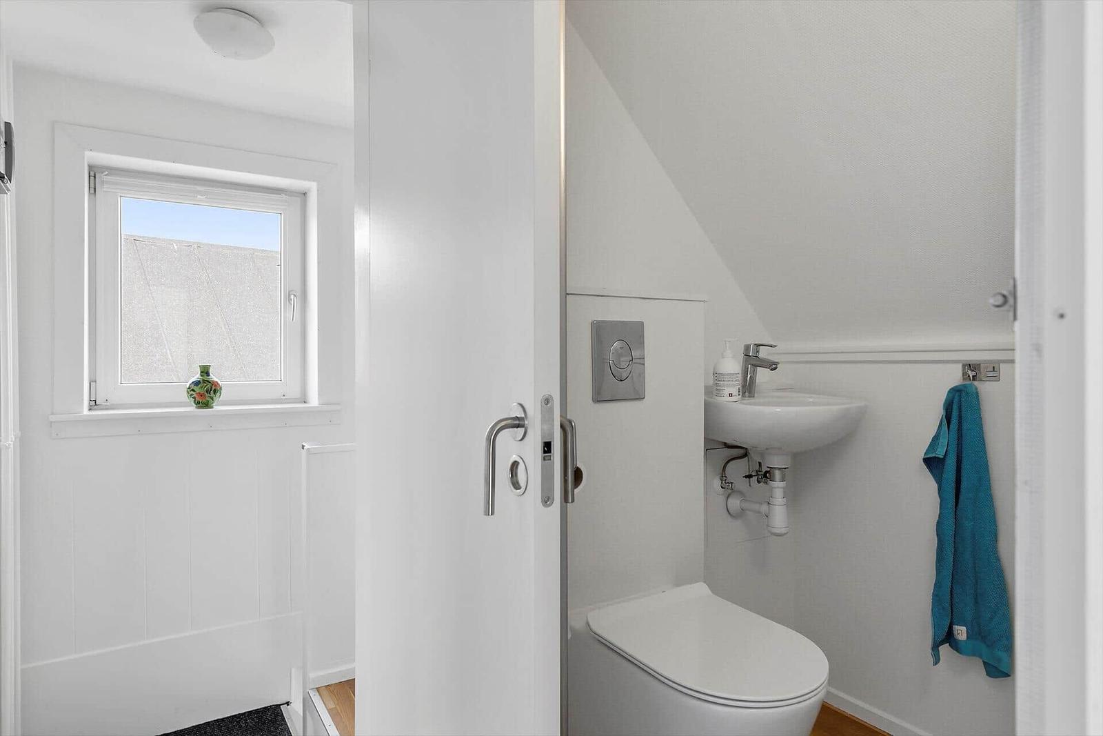 Badezimmer mit Toilette, Waschbecken und Fenster mit Blumentopf.