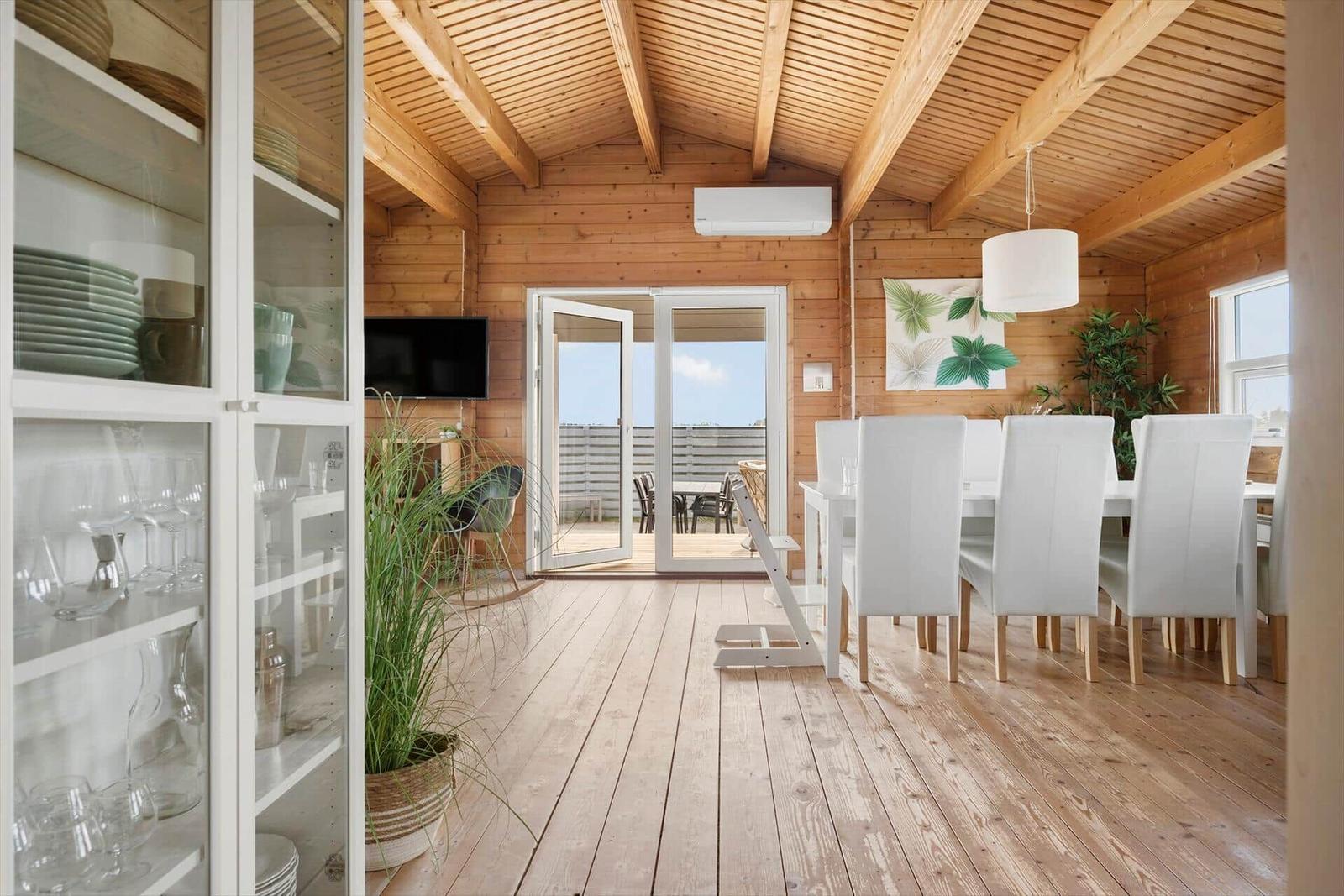 Dining room with white table, chairs, and wooden floor. Entrance to terrace with view of the sky.