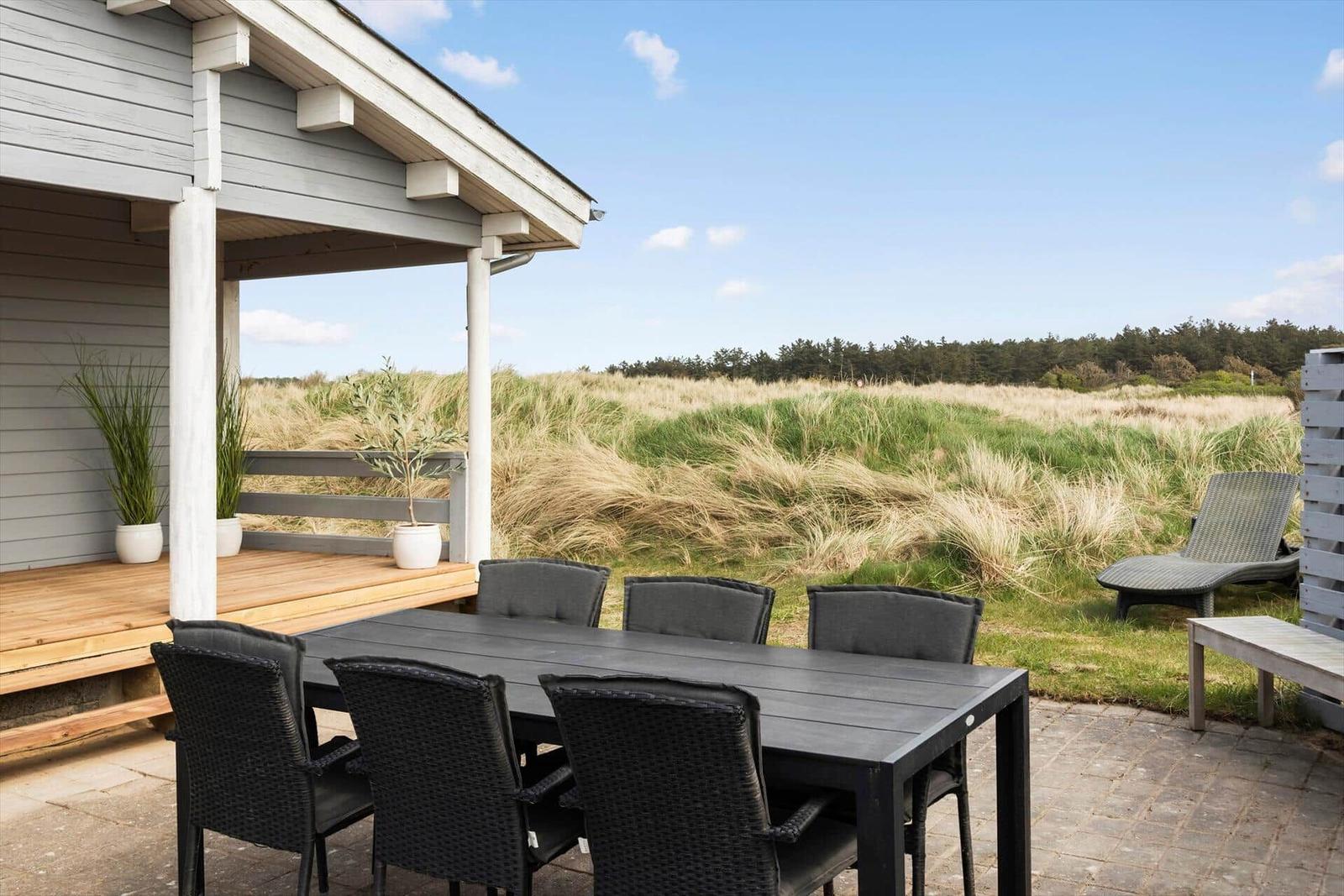 Terrace with table and chairs, view of grassland and forest.