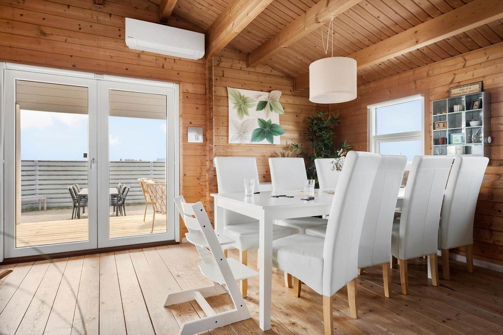 Dining room with white table and chairs, wooden walls, and terrace door.