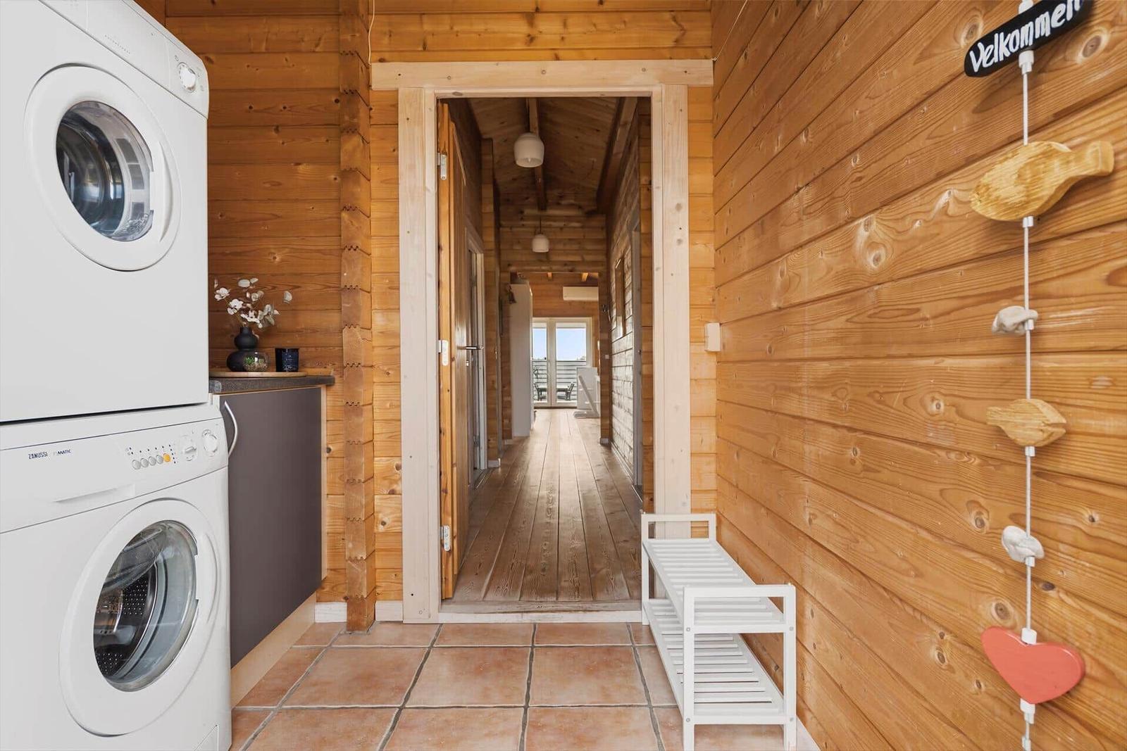 Washing machine and dryer in wooden house. Hallway leads to balcony.