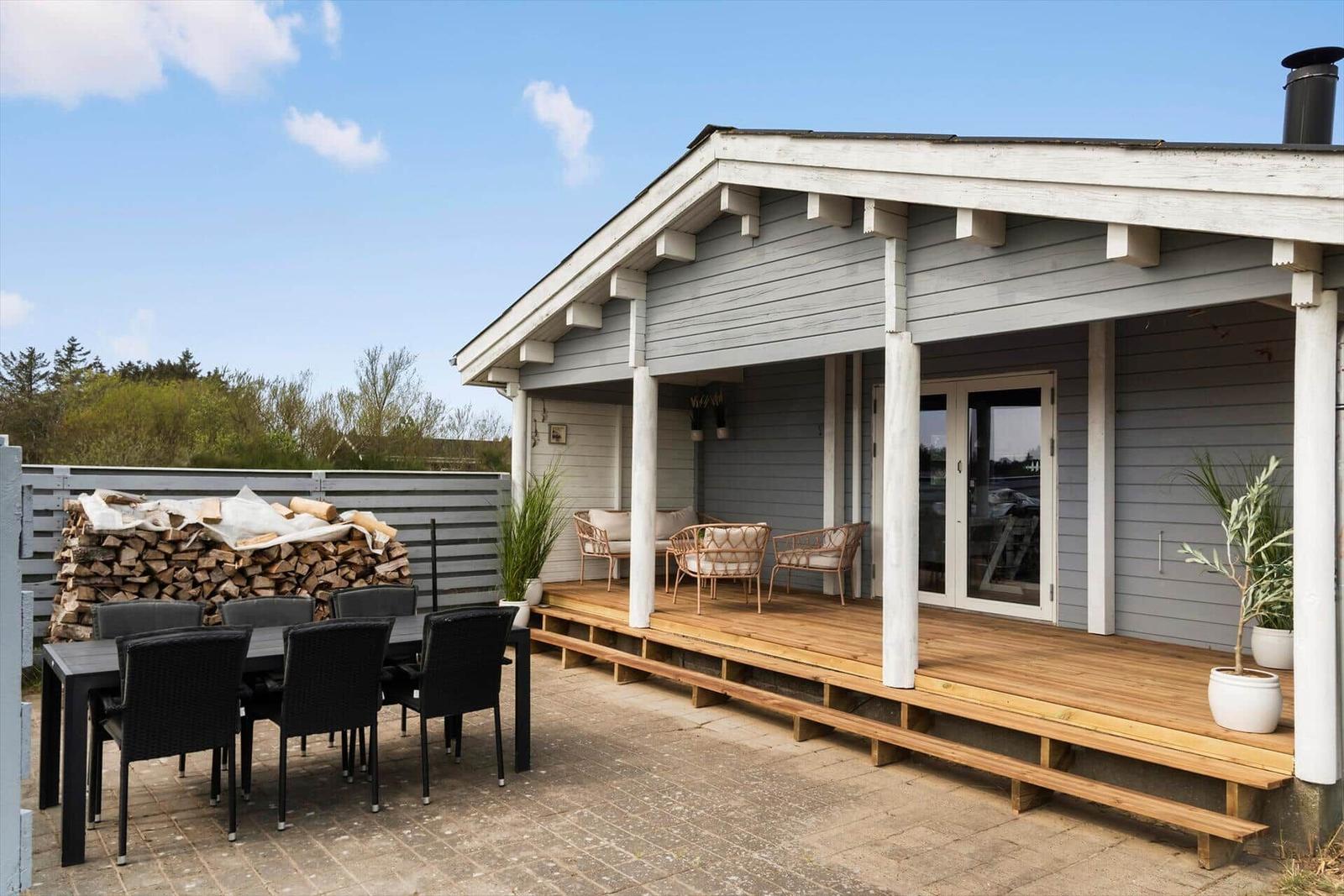 House with terrace, seating, and grill area. Wooden deck with garden furniture and firewood.
