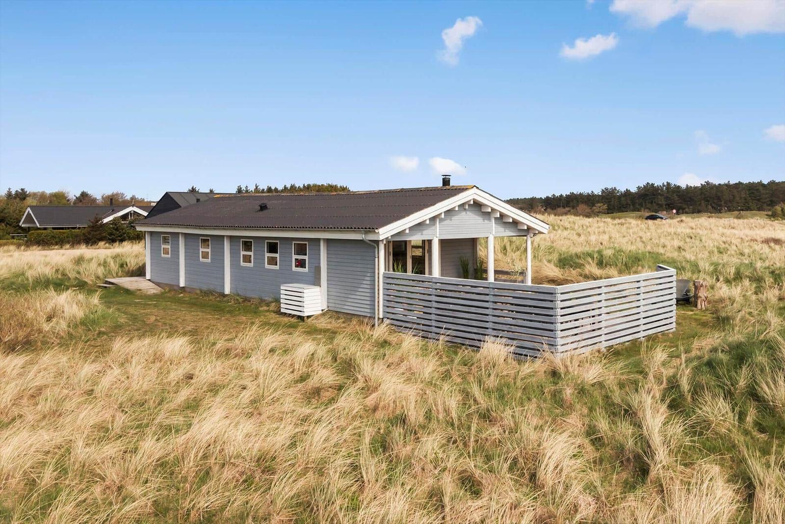 A gray vacation house with a terrace stands in a grassy landscape.