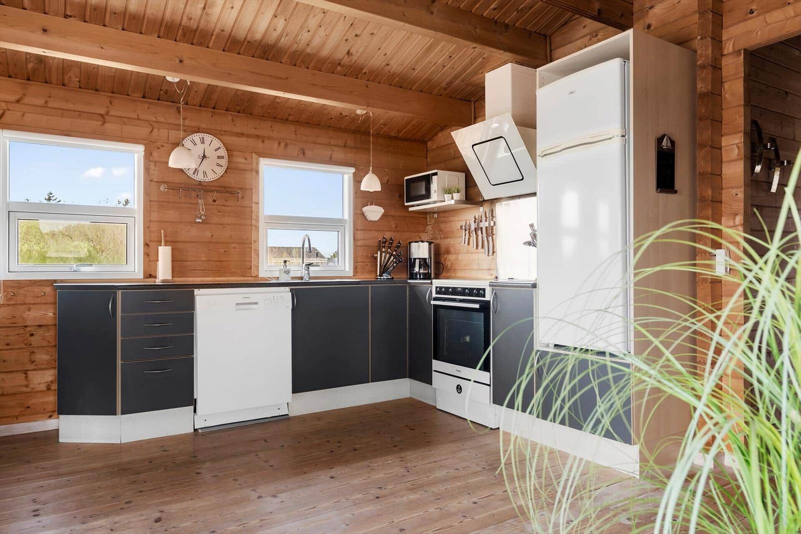 Kitchen with wooden walls, white appliances, and dark cabinets. Windows offer a view of the landscape.
