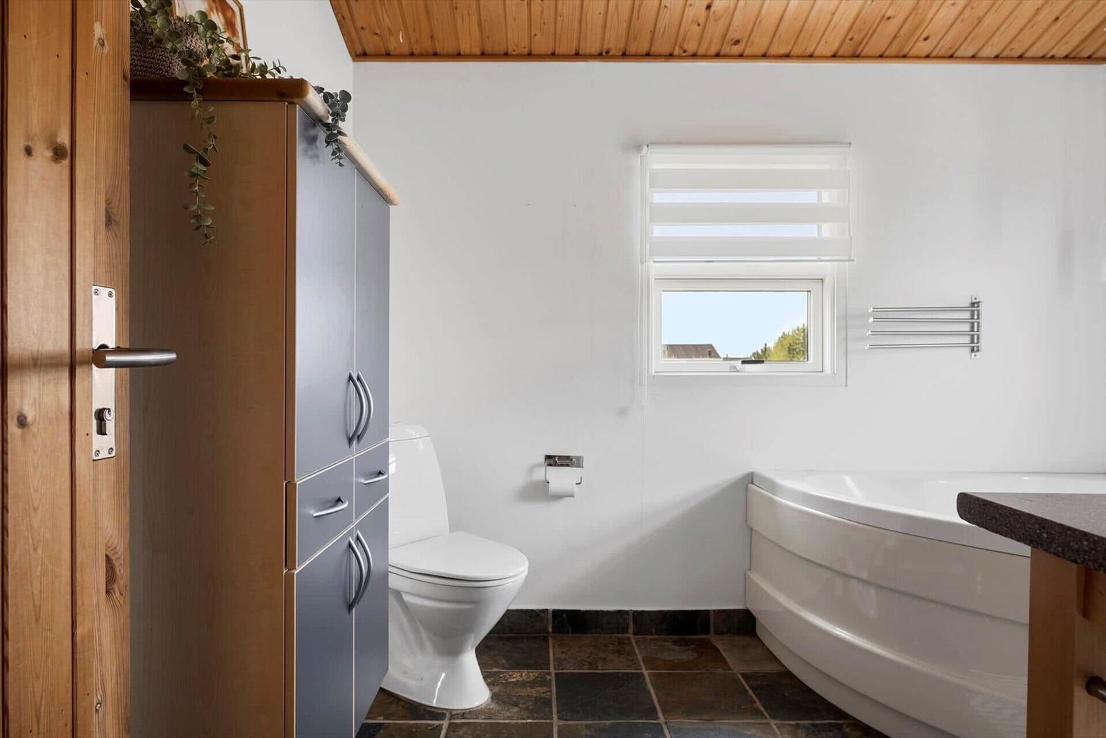 Bathroom with bathtub, toilet, and window with blinds.