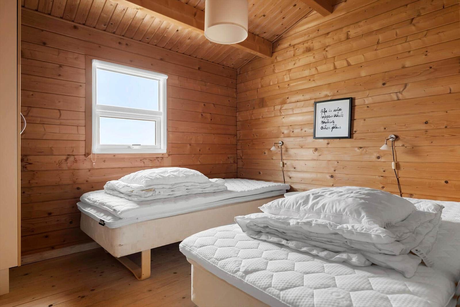 Two beds with white bedding in a wooden room with window and wall art.