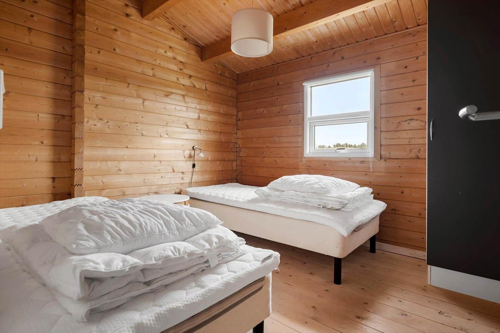 Two beds in a wooden house with window and closet.