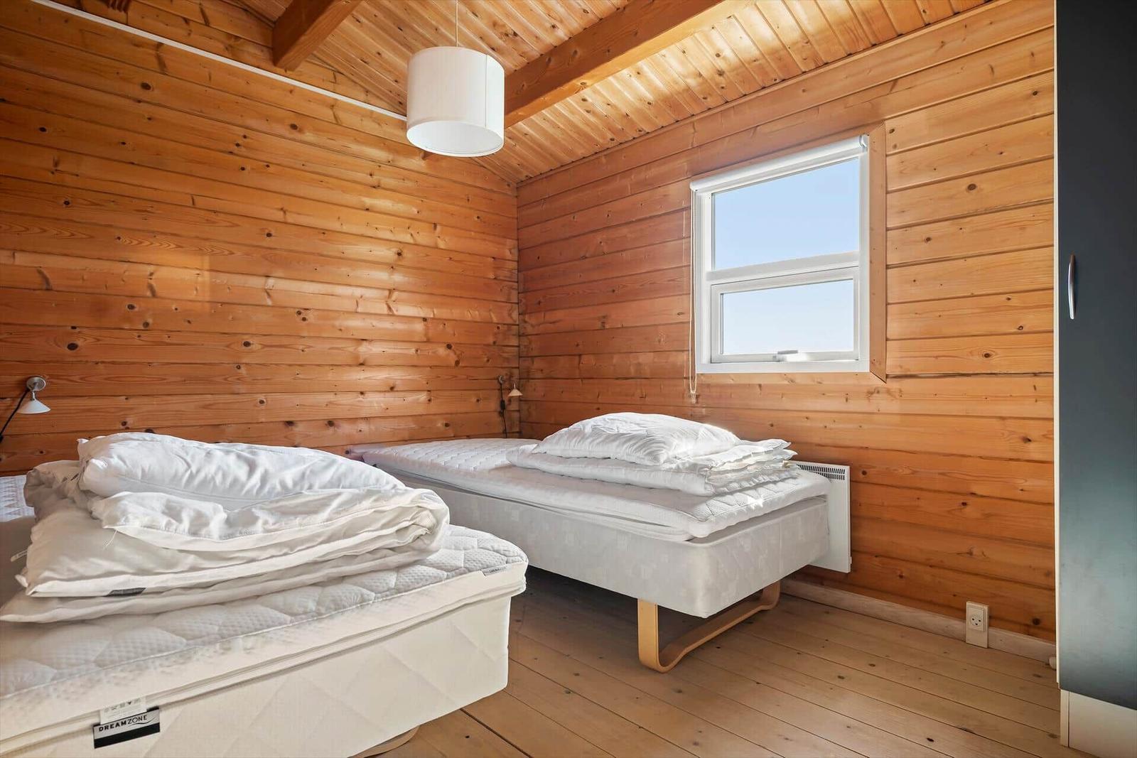 Two beds in a wooden room with window and ceiling lamp.