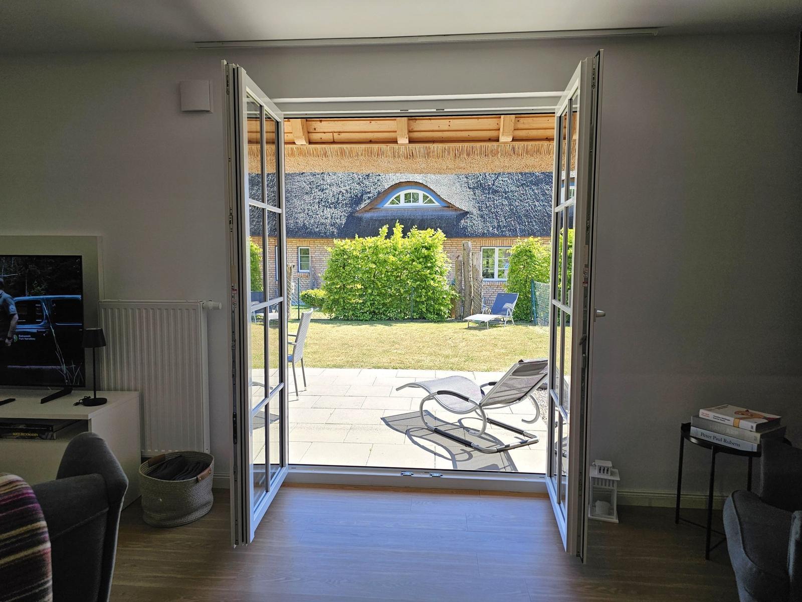 Durch offene Türen Blick auf Terrasse mit Liegen und grünen Hecken.