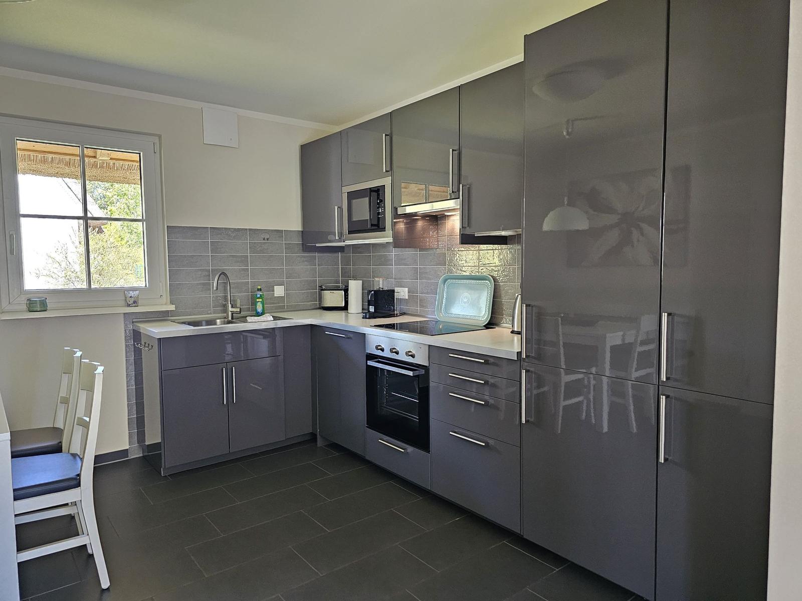 Moderne Küche mit grauen Schränken, Edelstahlgeräten und Fensterblick.