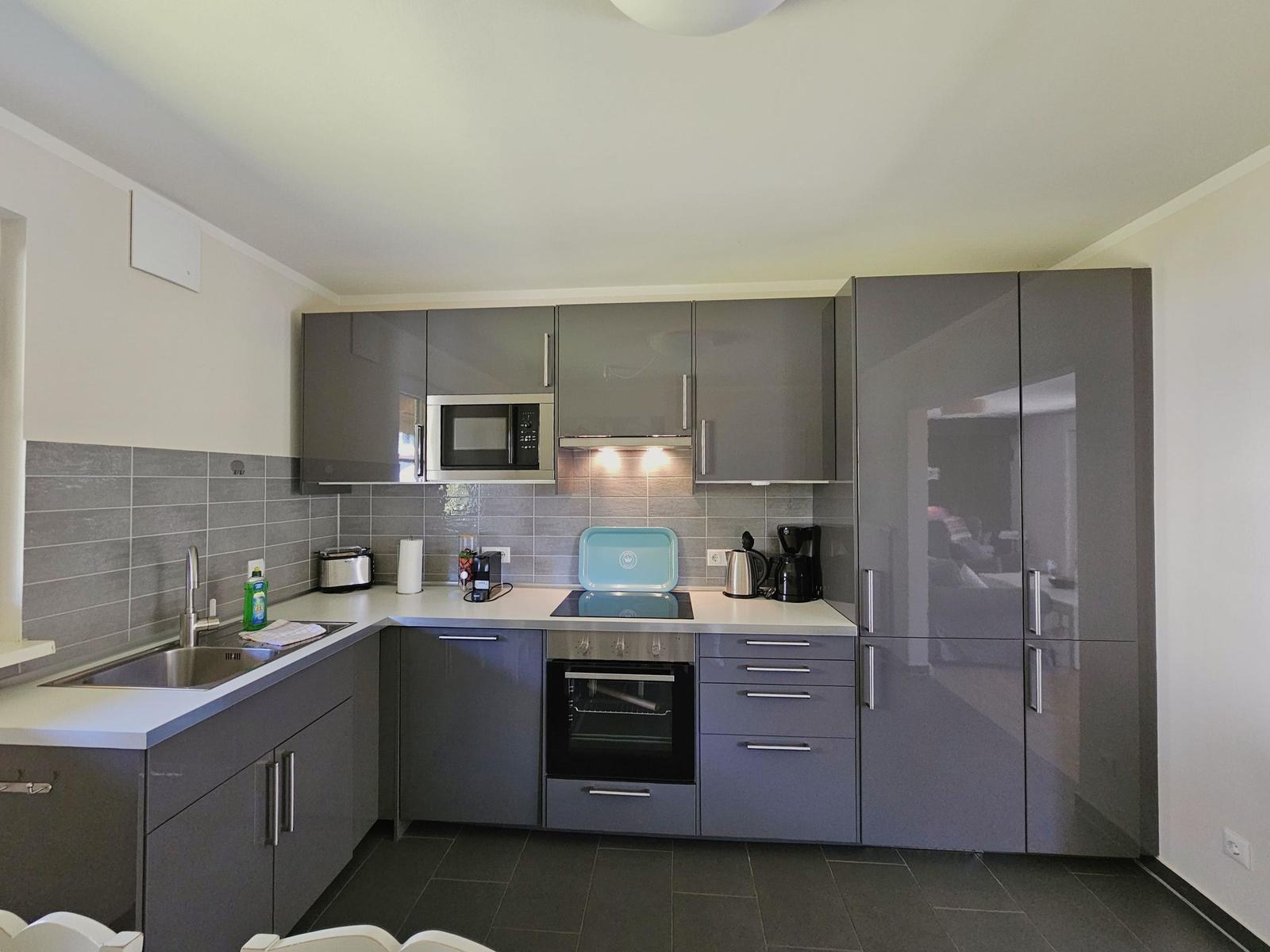 Moderne Küche mit grauen Schränken, Edelstahlgeräten und Arbeitsplatte.