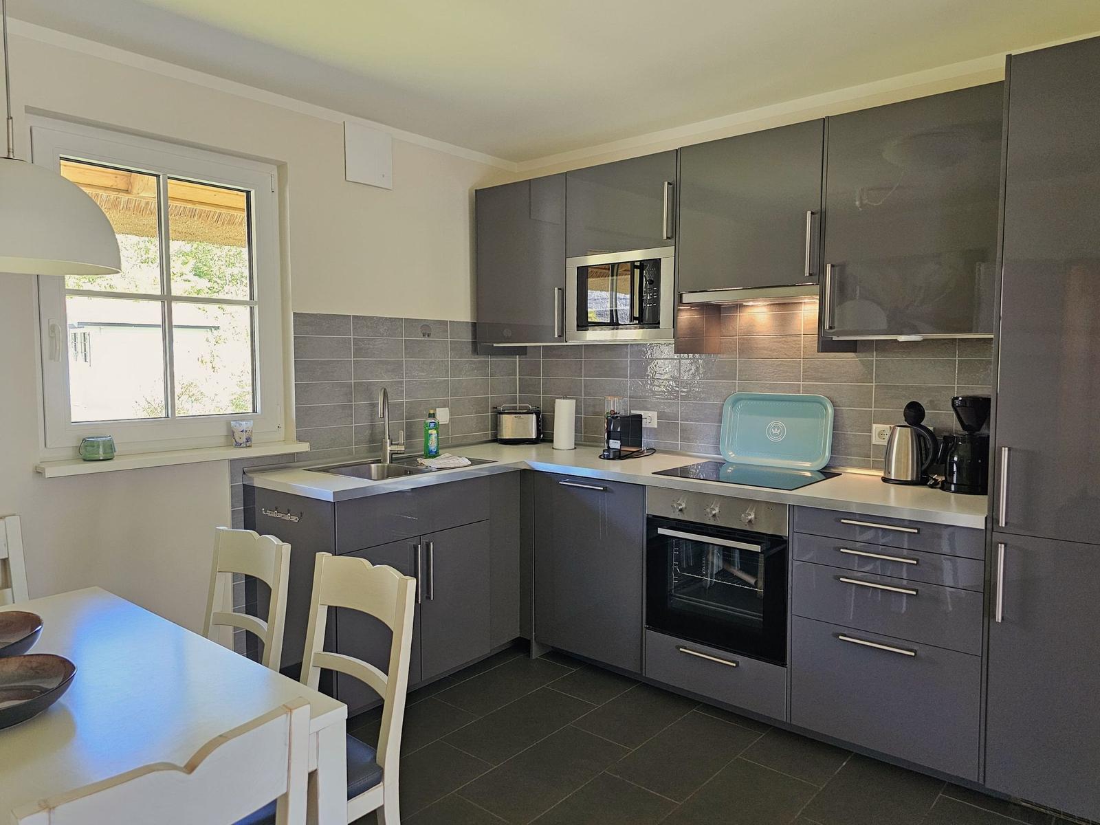 Moderne Küche mit grauen Schränken, Edelstahlgeräten und Fenster zum Garten.