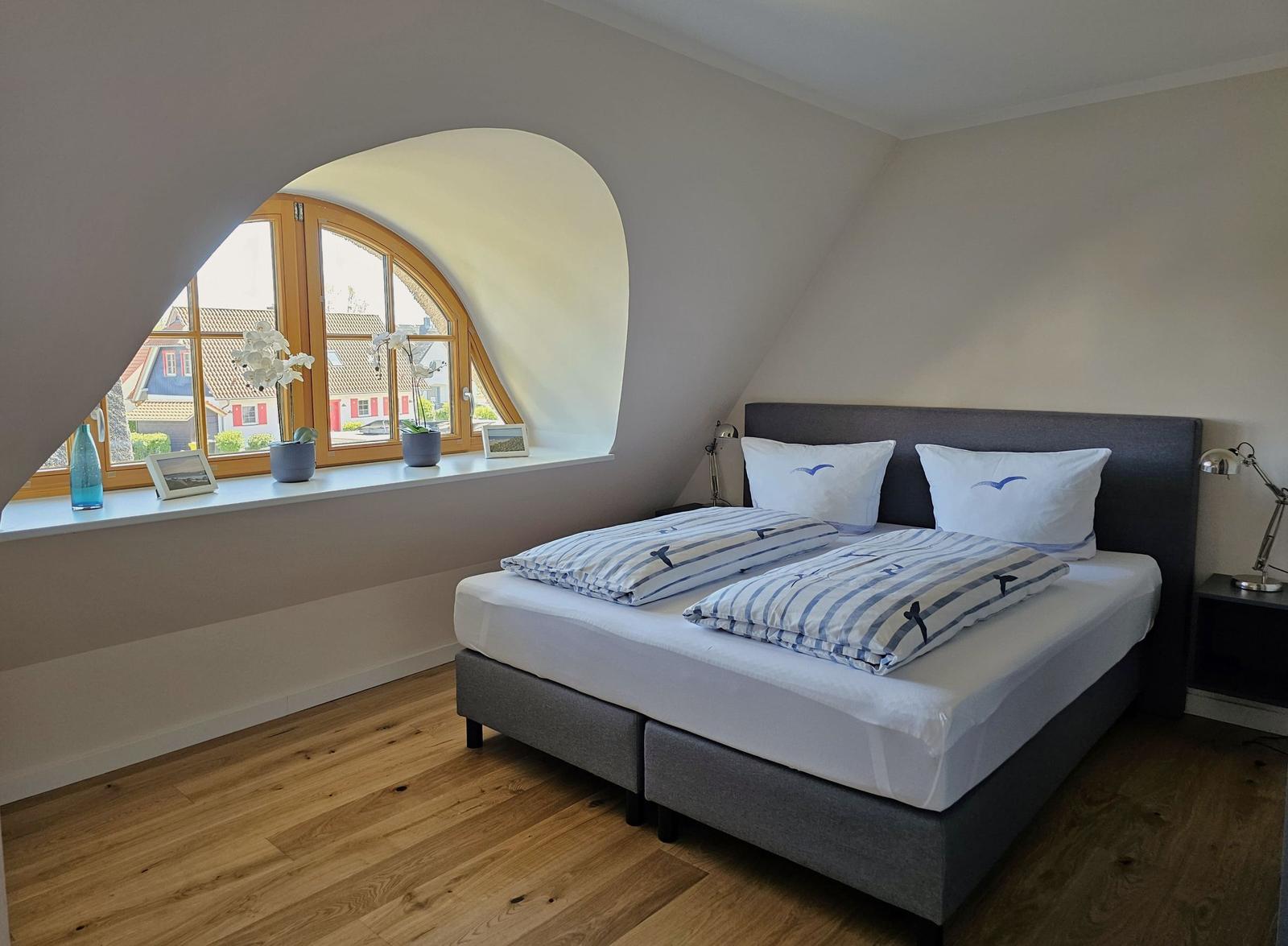 Schlafzimmer mit Dachschräge, großem Fenster und Bett mit Bettwäsche.