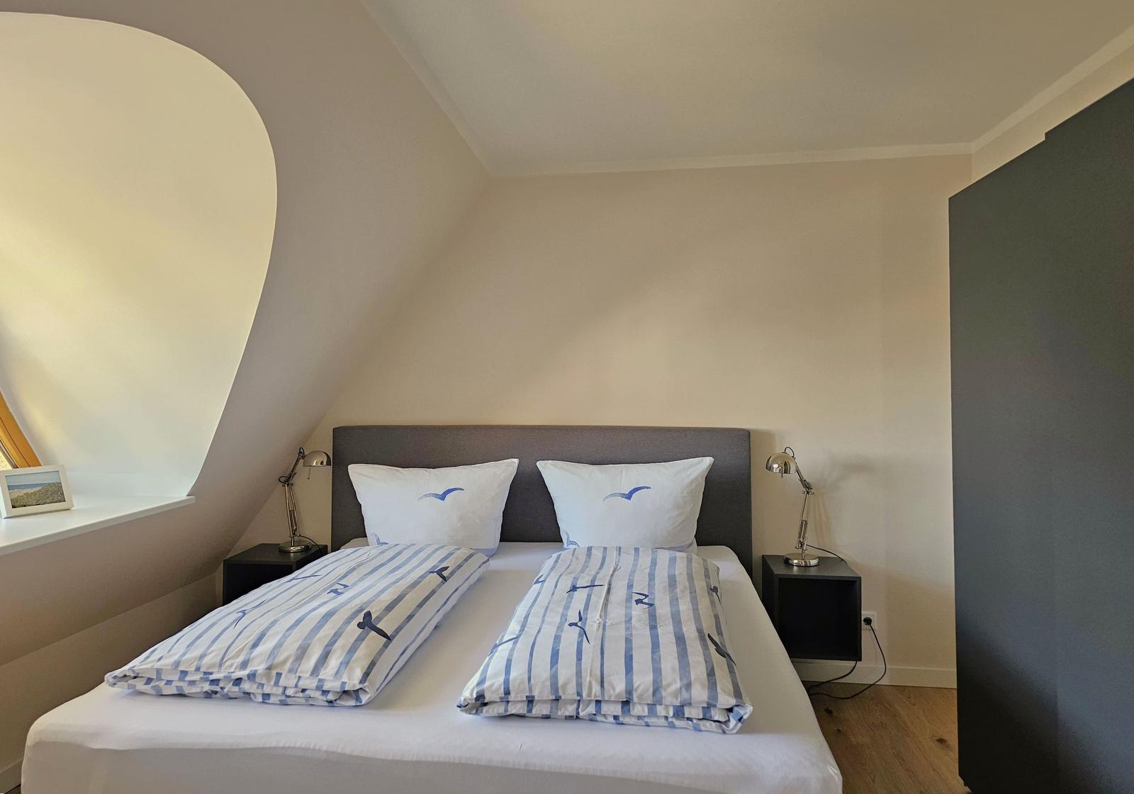 Schlafzimmer mit Doppelbett, zwei Nachttischen und einem Bogenfenster.