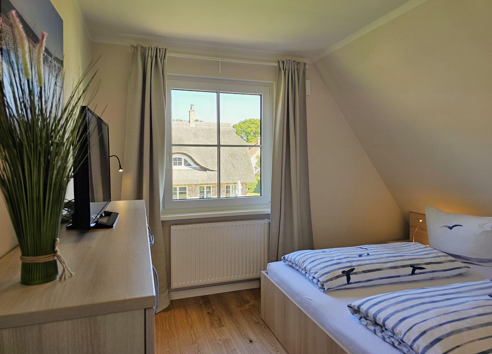 Schlafzimmer mit Doppelbett, Fenster und Schreibtisch.