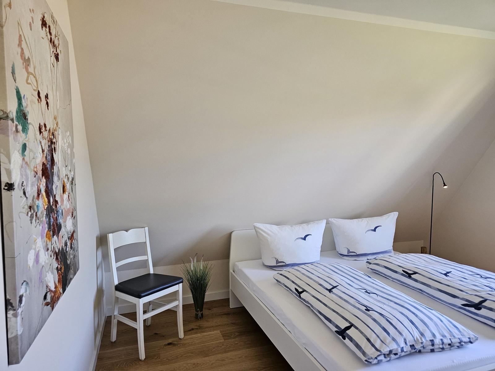 Schlafzimmer mit Doppelbett, Stuhl und Wandbild.