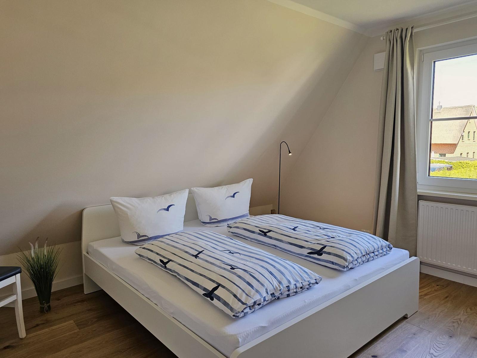 Schlafzimmer mit Doppelbett, Fenster und Holzboden.