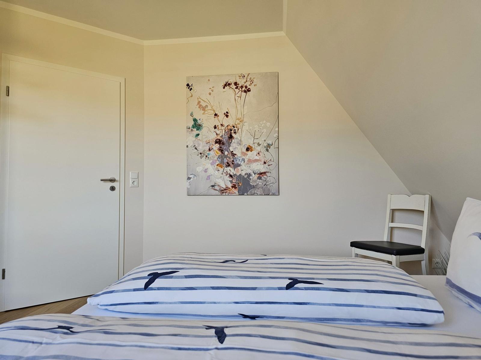 Schlafzimmer mit Bett, Stuhl und Wandbild unter Dachschrägen.