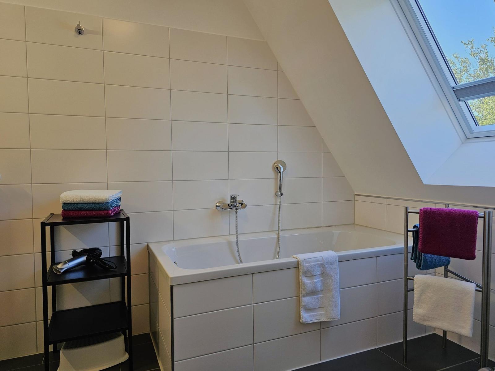 Badezimmer mit Badewanne, Dusche und Dachfenster. Handtuchhalter und -ständer.