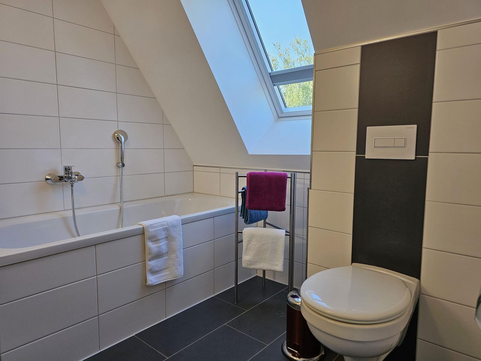 Badezimmer mit Badewanne, Dusche und Toilette unter Dachschrägen mit Dachfenster.