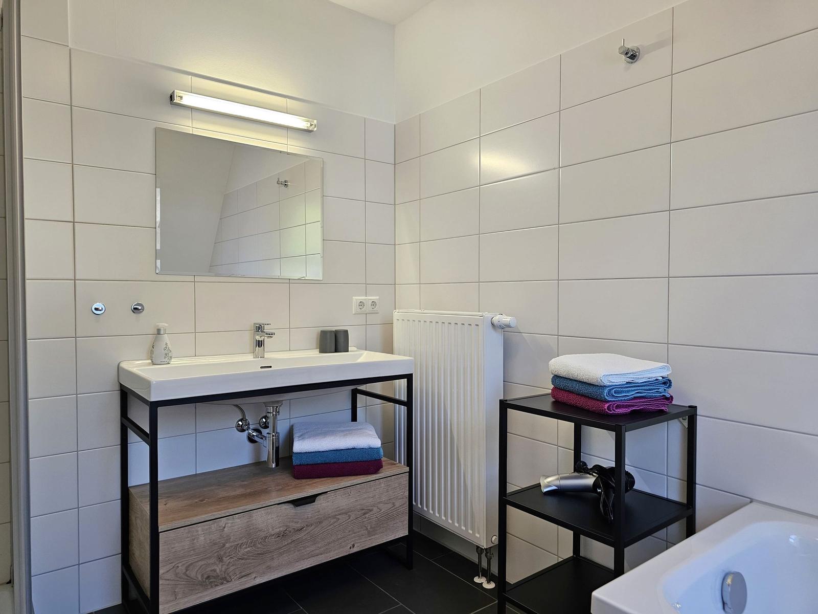 Badezimmer mit Waschbecken, Spiegel, Duschwanne und Handtüchern.