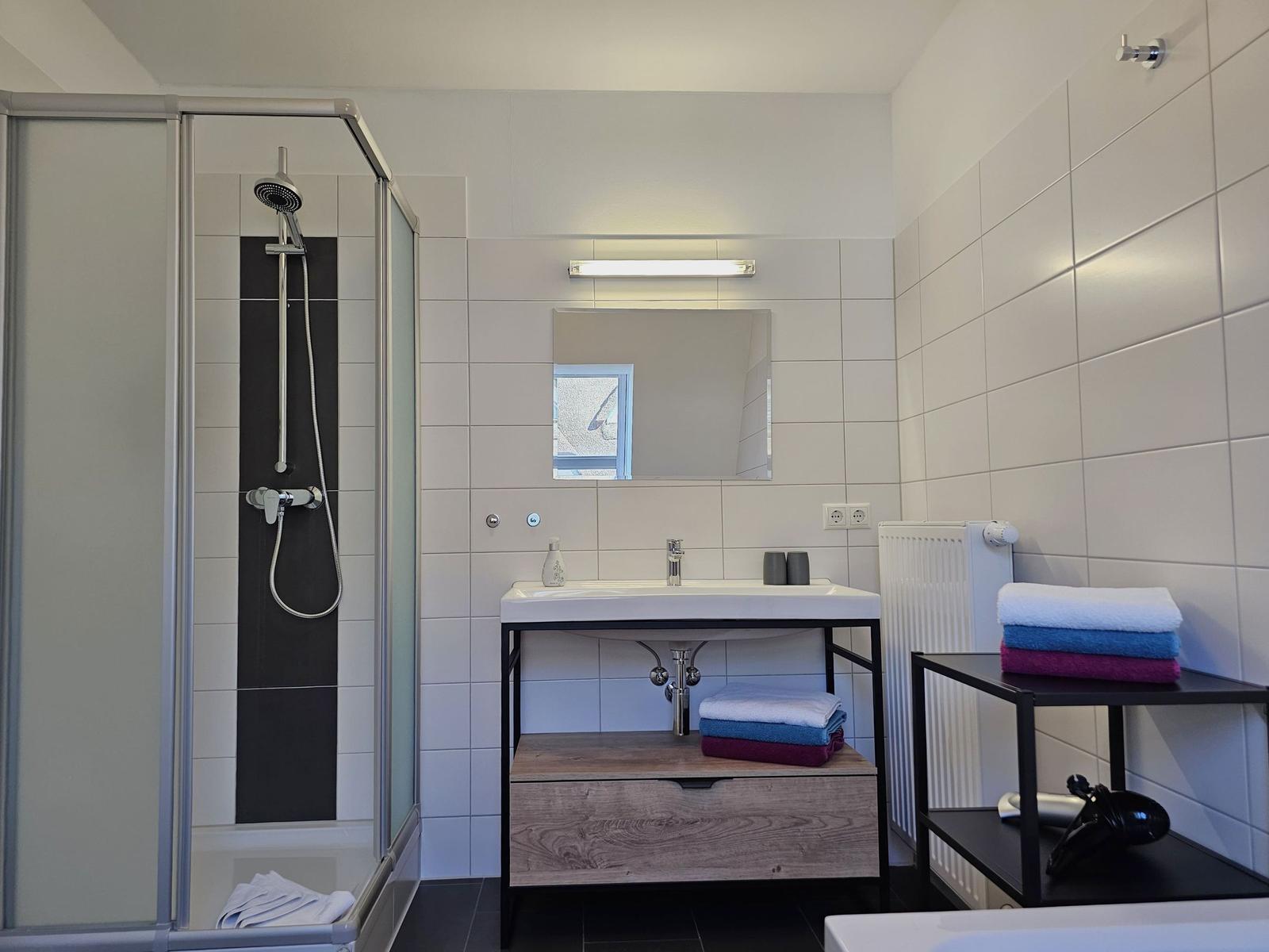 Badezimmer mit Dusche, Waschbecken und Handtuchständer.