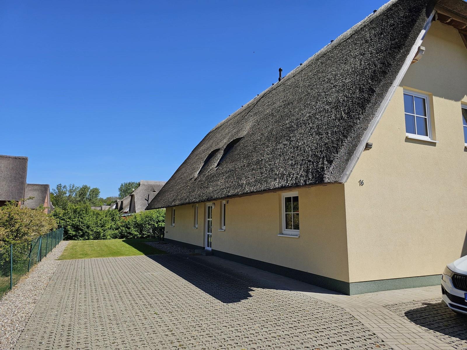 Ferienhaus mit strohgedecktem Dach und gepflastertem Vorplatz.