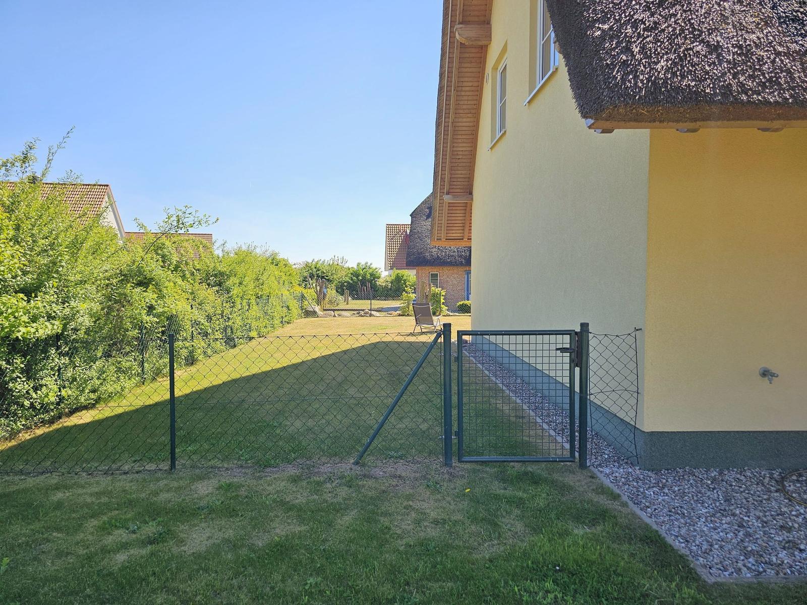 Hinterhof mit Gartenzaun und Tor. Gelber Hauswand und Dachreep.