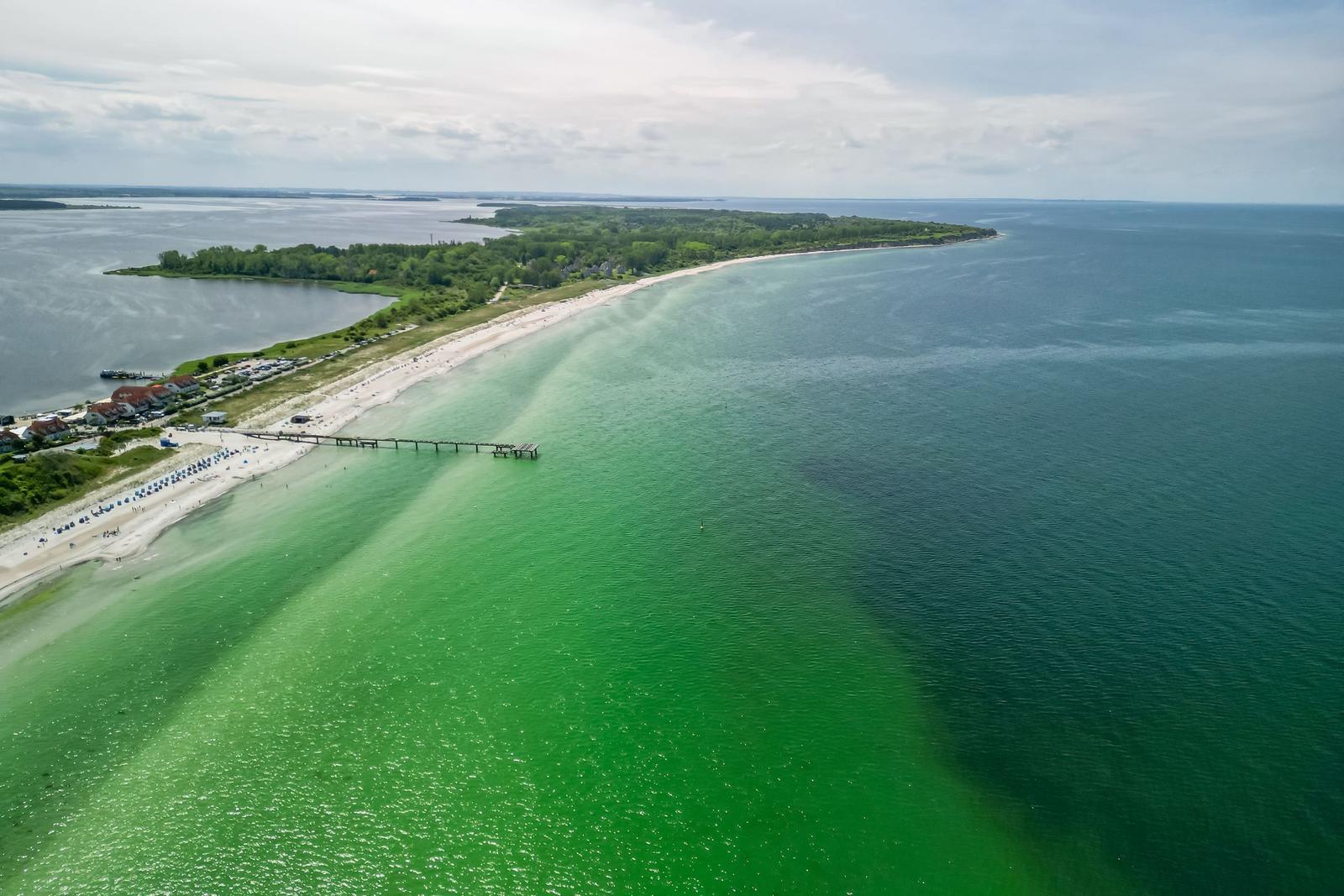 Aerial view of a long beach with clear water and a pier.