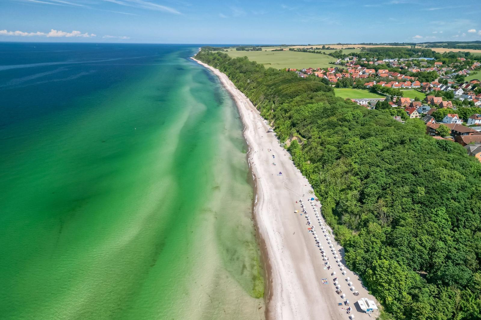 Strand mit kristallklarem Wasser und grüner Landschaft neben einem Dorf.