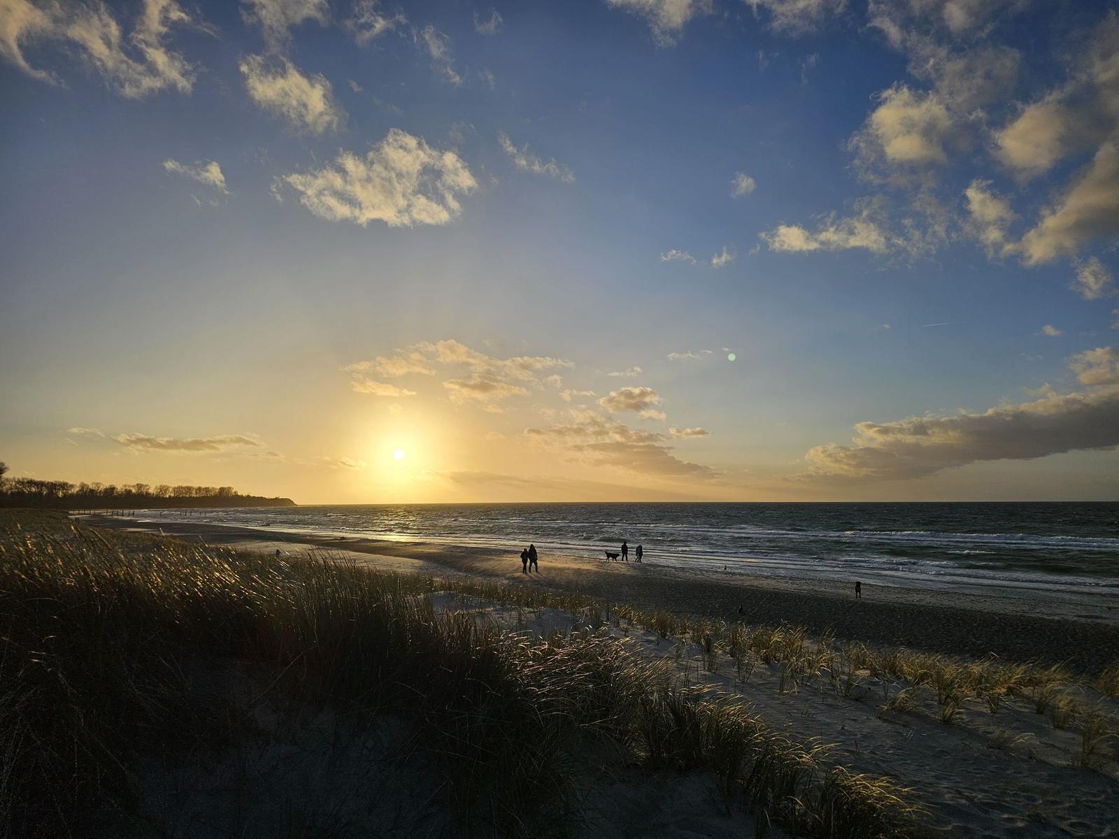 Sonnenuntergang am Strand mit Wellen und Menschen in der Ferne.