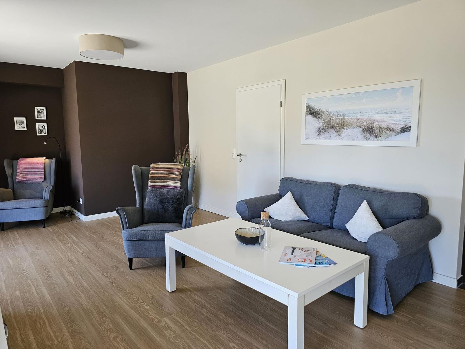 Wohnzimmer mit Sofa, zwei Sesseln, Tisch und Wandbild.