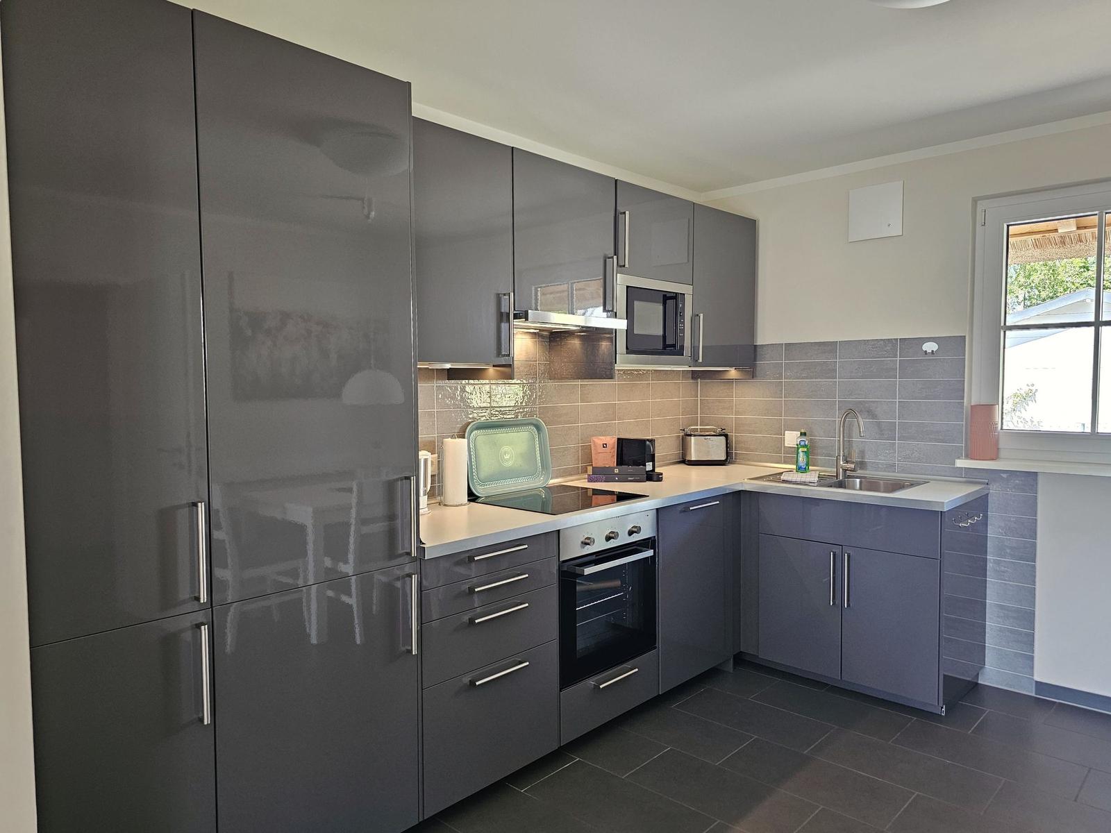 Moderne Küche mit grauen Schränken, Edelstahlspüle und integriertem Backofen.