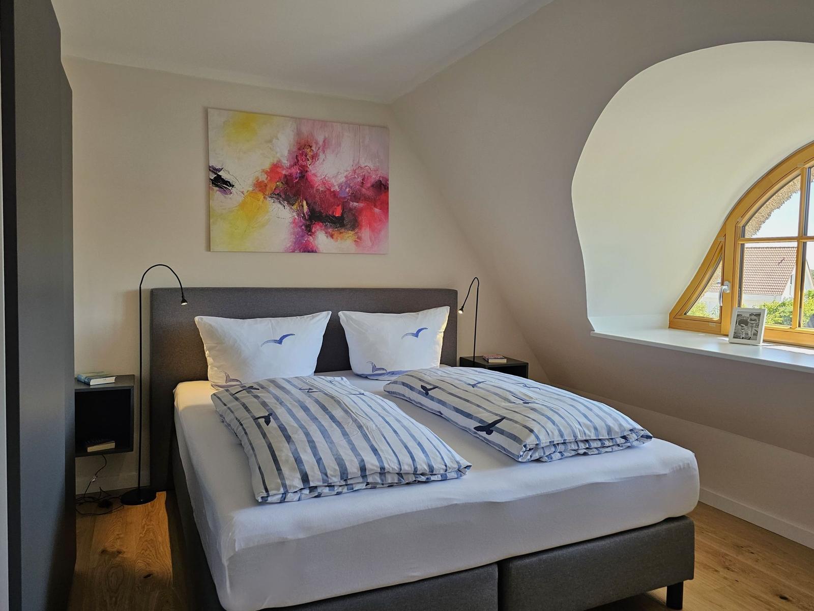 Schlafzimmer mit Doppelbett, Wandbild und Bogenfenster.