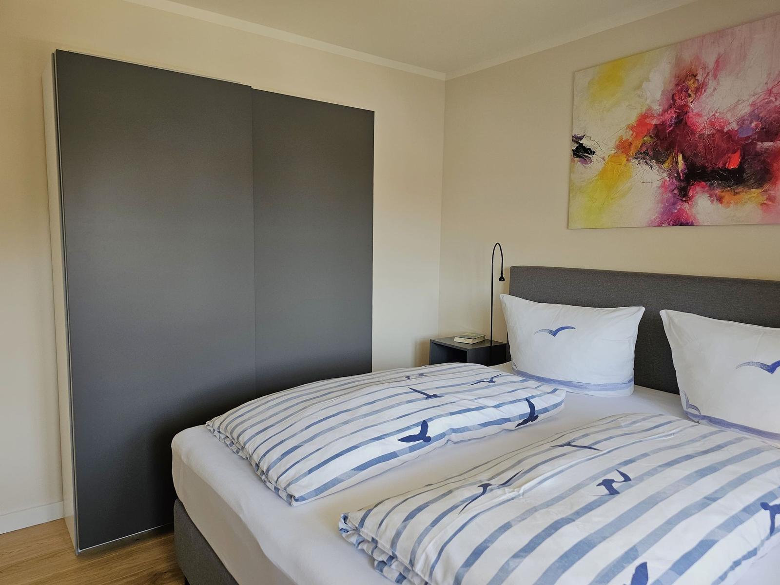 Schlafzimmer mit Doppelbett, Kleiderschrank und Wandbild.