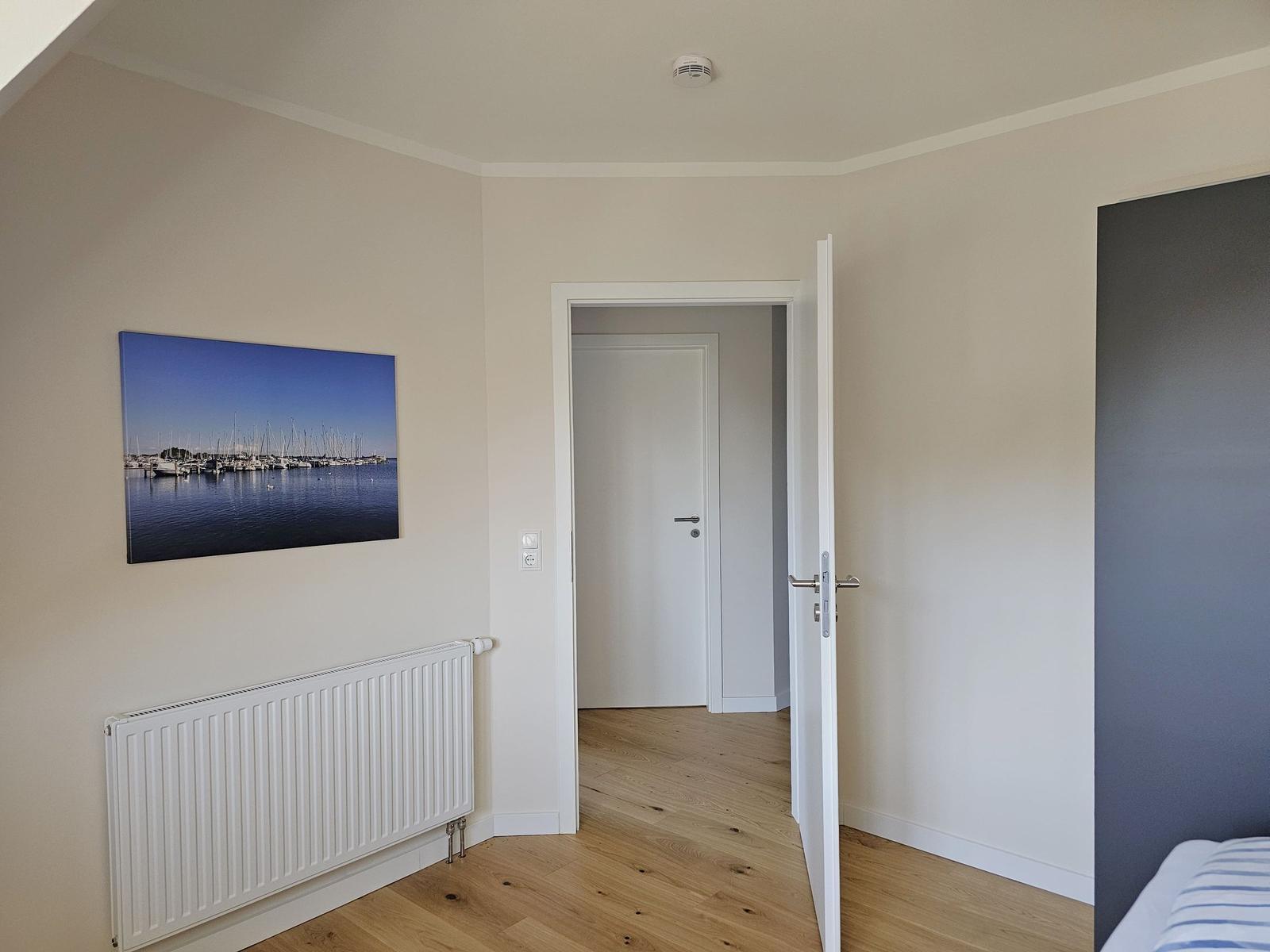 Schlafzimmer mit Holzboden, Wandbild und offener Tür zum Flur.