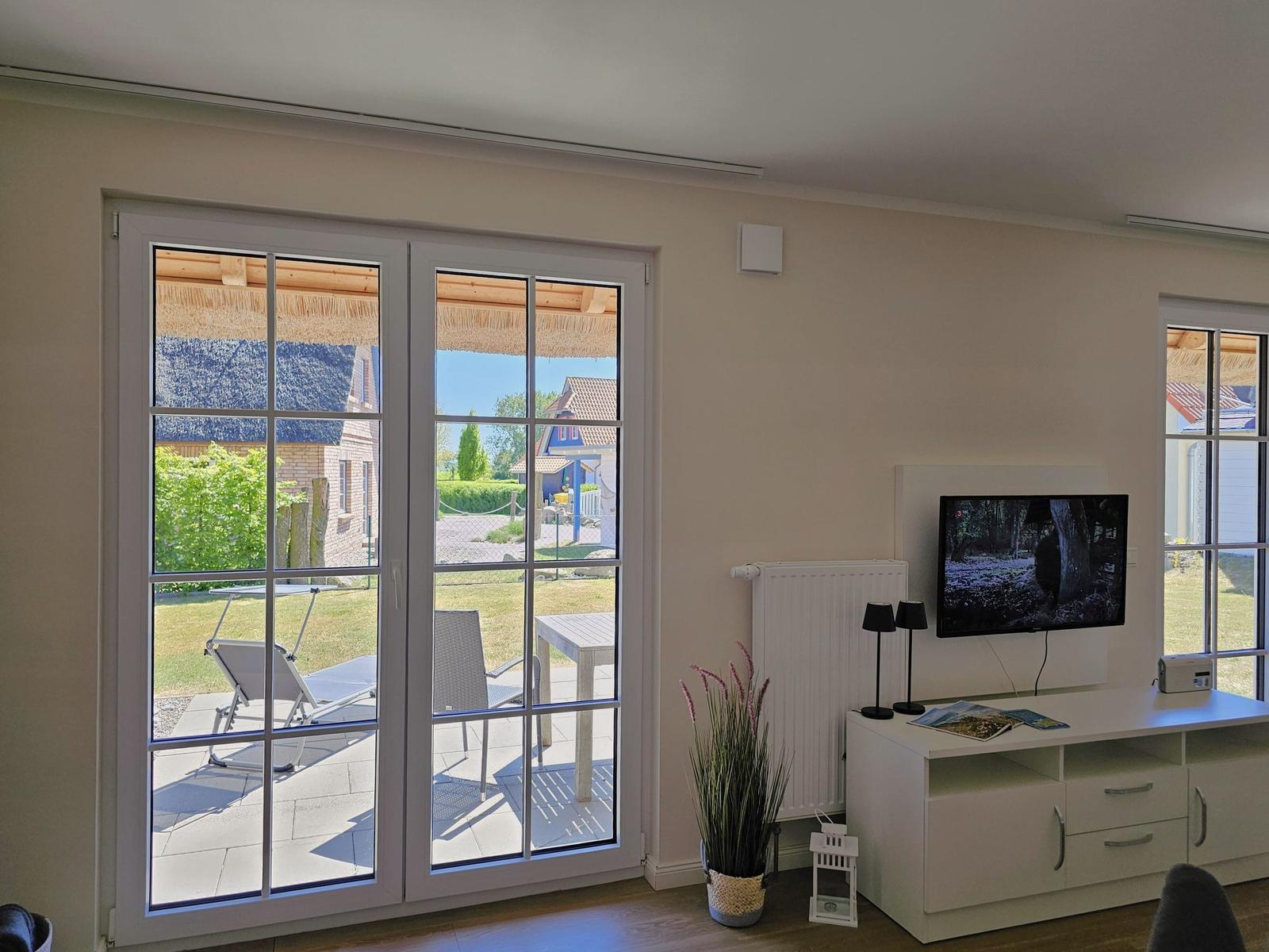 Wohnzimmer mit TV und Blick auf Terrasse mit Garten.