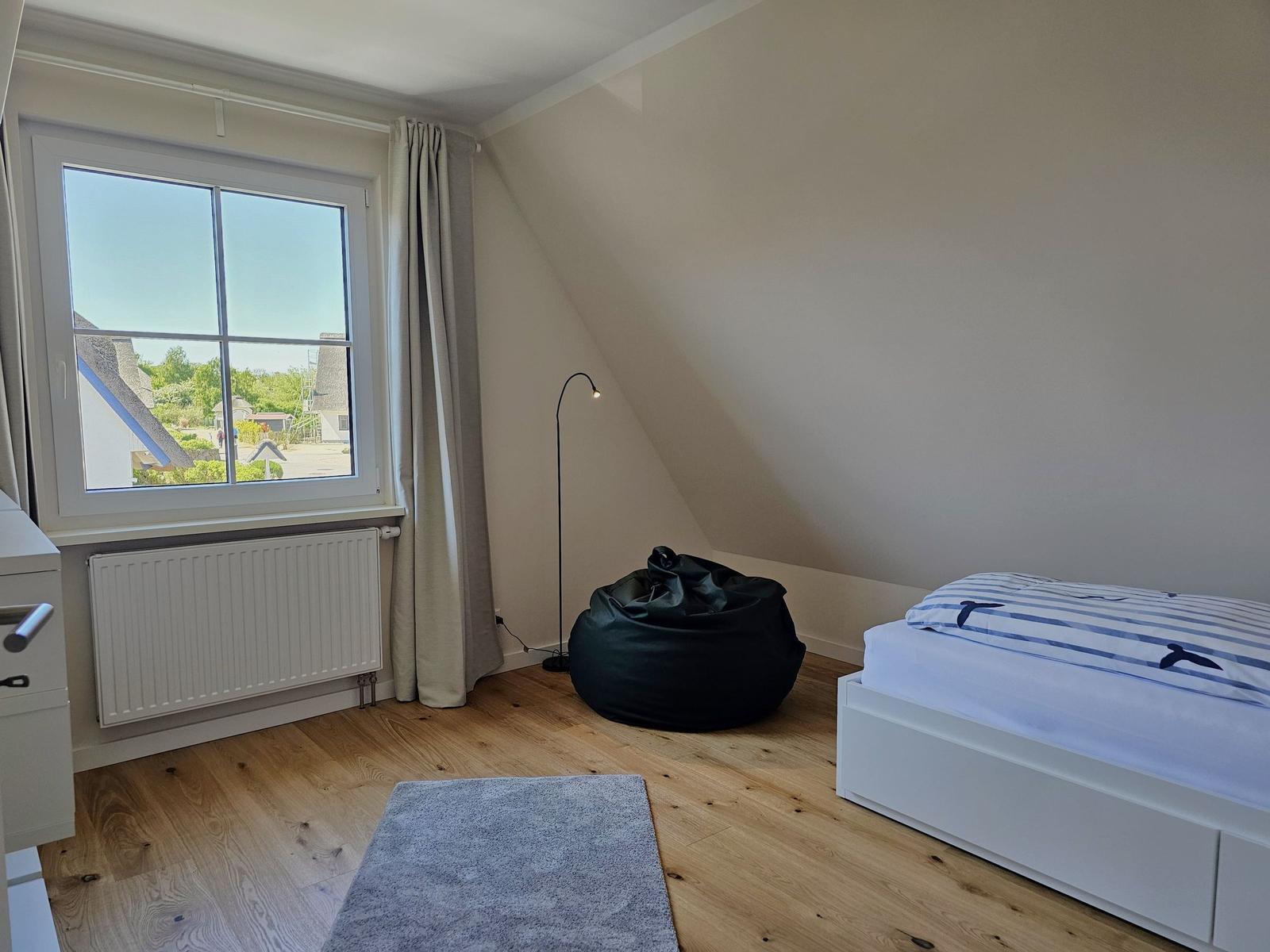 Schlafzimmer mit Dachschräge, Bett, Sitzsack und Fenster mit Blick.